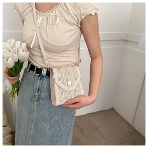 Detail of hand-woven straw phone bag with floral embroidery and crossbody strap