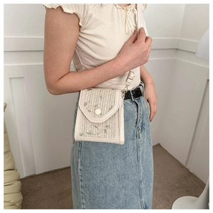 Close-up of beige woven crossbody bag featuring green leaf embroidery and flap closure