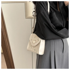 Detail of woven crossbody bag featuring floral embroidery and white leather strap on model