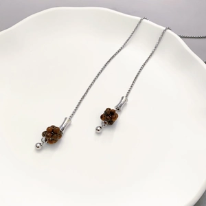 Long silver chain tassel earrings with brown beads on a minimalist white ceramic plate