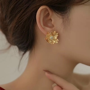 Detail of 18K gold daisy stud earring with zircon center and brushed metal petals