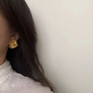 Detail of 18K gold-plated daisy earrings with zircon inlay worn by a model