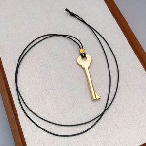 Gold-plated key pendant necklace on black cord over a textured white linen background