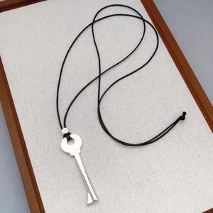 Minimalist silver key pendant necklace with black cord on a textured wooden tray