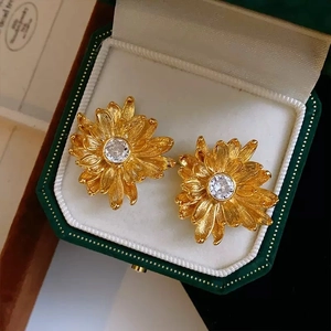 Macro detail of gold daisy earrings with brushed petals and zircon center in jewelry box