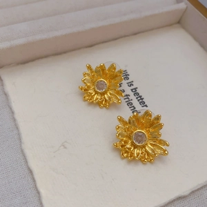 Detail of gold daisy earrings with cubic zirconia and butterfly backings on paper
