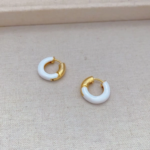 Detail of gold-plated hoop earrings with white enamel finish and polished texture