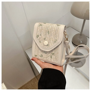 Macro detail of beige woven straw phone bag featuring delicate green leaf embroidery