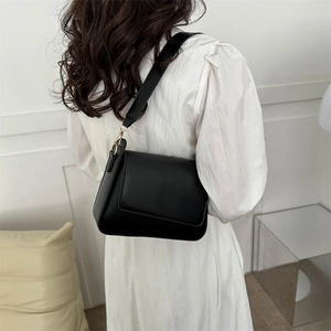 Minimalist black faux leather shoulder bag with gold hardware shown on a model