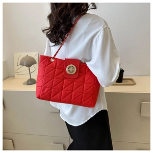 Dettaglio della borsa tote rossa trapuntata con emblema dorato e tracolla a catena su modella