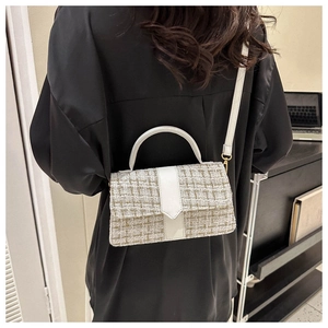 Detail of tweed crossbody bag with white leather trim worn by a model in black outfit