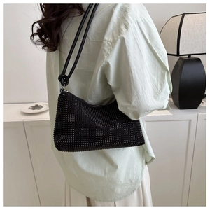 Side view of black rhinestone underarm bag worn by model in a minimalist interior