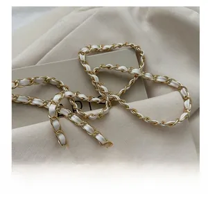 Detailed close-up of the woven gold metal chain strap with white leather threading
