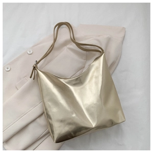Detail of high-gloss metallic gold tote bag with slender straps on beige background