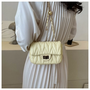 Détail d'un sac bandoulière matelassé jaune clair avec chaîne dorée sur robe blanche