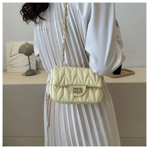 Détail d'un sac à main matelassé jaune clair avec chaîne dorée et fermoir rotatif en métal
