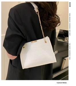 Detail of white crocodile embossed shoulder bag with gold chain strap on model