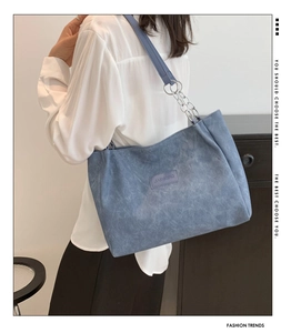 Detail of blue washed denim tote bag with silver chain strap and leather logo patch