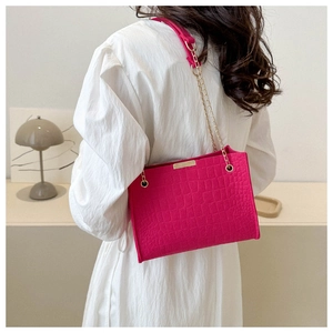 Detail of hot pink crocodile-embossed bag with golden chain strap on white dress
