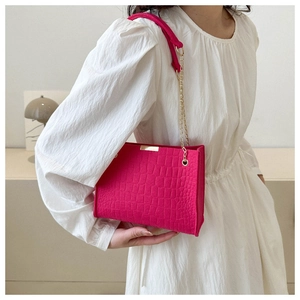 Detail of a bright fuchsia small square bag with crocodile pattern and golden chain strap