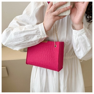 Close-up of pink felt square bag with crocodile pattern and golden chain strap detail