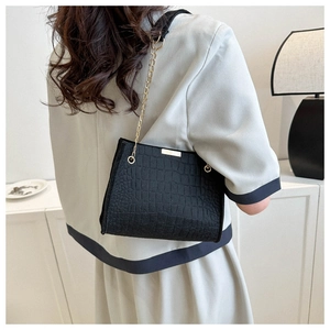 Detail of black crocodile pattern shoulder bag with elegant gold chain and metal trim