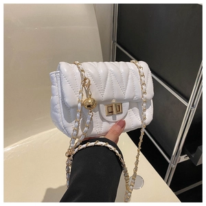 Gros plan d'un sac matelassé blanc avec fermoir doré et pendentif boule en métal