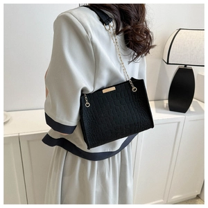 Detail of black crocodile texture bag with gold chain strap on shoulder