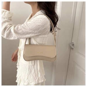 Close-up of beige leather baguette bag with gold lettering on a white lace dress