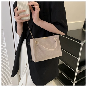 Detail of light beige crocodile pattern square bag with gold chain strap on model