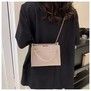 Detail of beige crocodile pattern mini bag with gold chain strap on black blazer