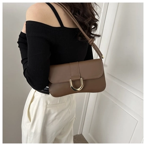 Close-up of dark brown leather underarm bag with gold horseshoe buckle on model