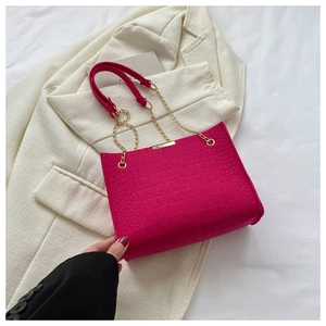 Detail of hot pink crocodile texture leather with gold chain strap on a small tote bag