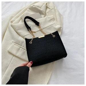 Detail of black crocodile texture handbag with gold metal bar and chain strap