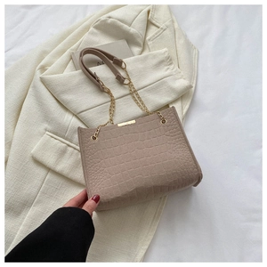 Detail of crocodile embossed leather bag with gold metal chain strap on white blazer