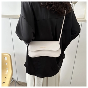 Detail of white leather shoulder bag with gold lettering shown on model with yellow chair