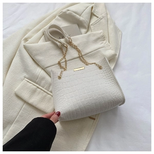 Detail of white crocodile pattern felt bag with gold chain strap on a beige blazer