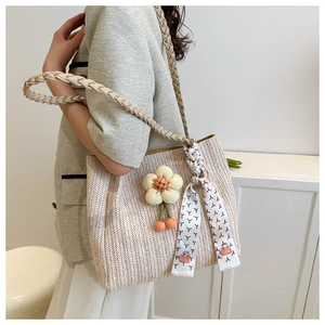 Detail of straw woven tote bag featuring thick twisted straps and floral charm