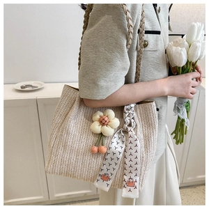 Detail of woven straw tote bag with sunflower charm and geometric patterned silk scarf