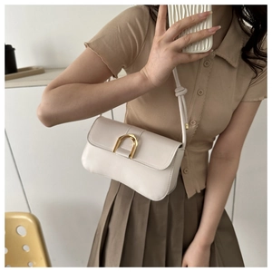 Chic beige leather underarm bag with gold horseshoe buckle shown on model in soft light
