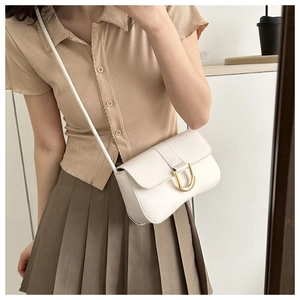 White leather crossbody bag with gold U-shaped buckle styled on a minimalist model outfit