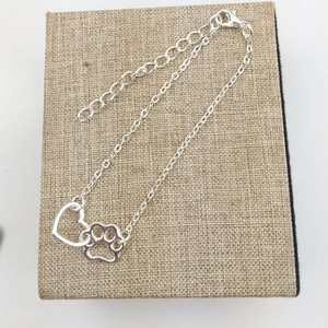 Detail of silver alloy bracelet featuring hollow heart and dog paw charms with lobster clasp