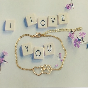 Close-up of gold alloy bracelet featuring hollow heart and dog paw charms on a floral background