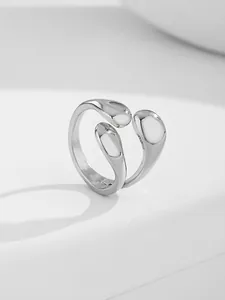 Macro shot of silver-tone alloy nail ring with smooth bean shapes on white minimalist stand
