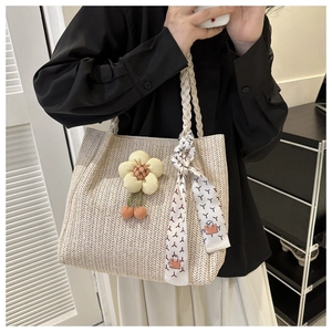 Detail of woven straw tote bag with braided handles, colorful scarf and flower charm