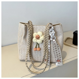 Detailed macro of woven straw tote bag featuring yellow fabric flower and printed silk ribbon