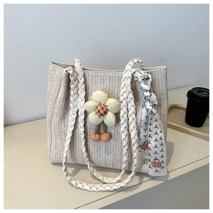Detail of straw woven tote bag featuring yellow plush flower and decorative silk ribbon scarf