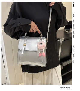 Gros plan d'un sac à bandoulière argenté métallisé avec un charm poupée en peluche rose