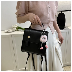 Détail d'un sac en cuir noir avec boucle dorée et breloque en peluche rose