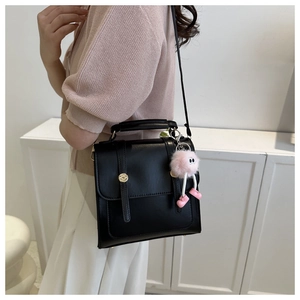 Vue détaillée d'un sac bandoulière en similicuir noir avec sangles et pompon rose